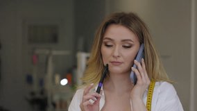 Woman fashion designer, is engaged in phone conversation in her sewing studio. Dressed in a professional yet casual style holds a pen and has tape measure draped over her shoulders. - Powered by Shutterstock - Get 15% off with code: PIKWIZARD15