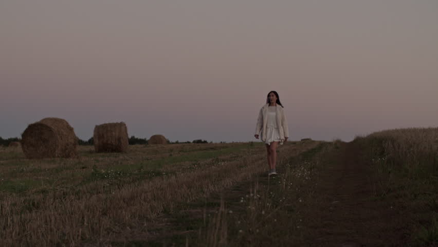 Smiling young woman walking on rural field at sunset