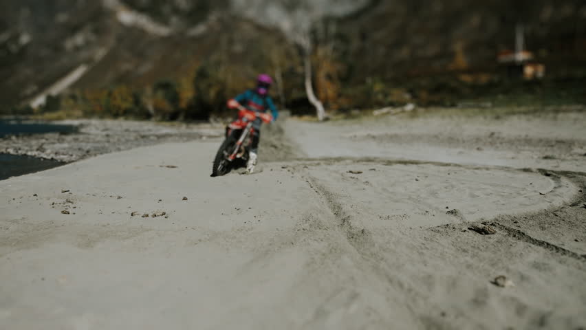 An experienced motocross racer rides around in the sand, close-up. Sand flies from under the motorcycle wheel into the camera.