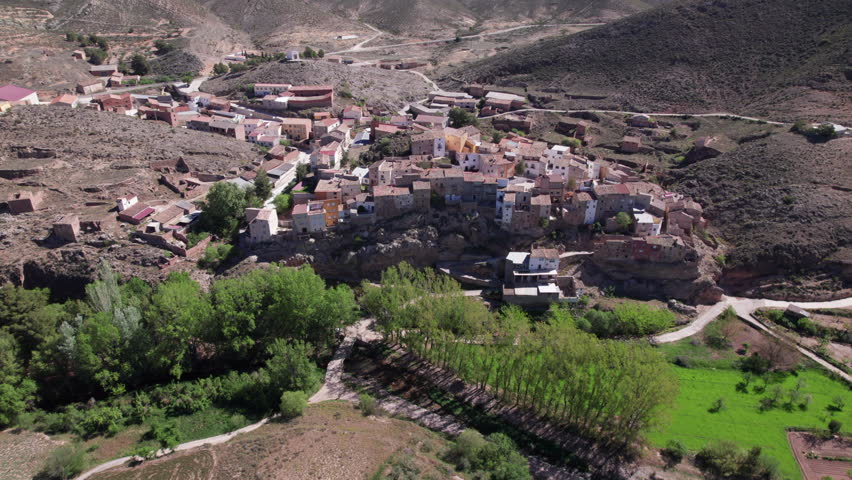 Aerial view of a small town with closely packed buildings, winding roads, and surrounding green patches in a hilly landscape