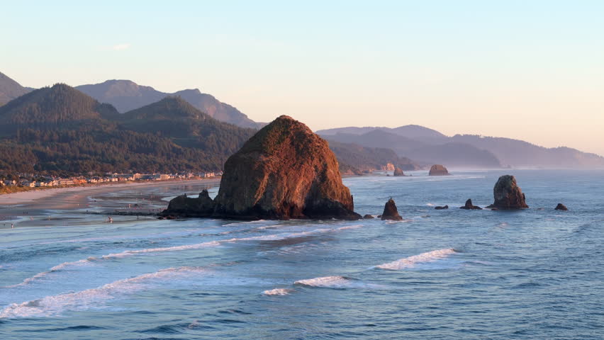 Experience the breathtaking and stunning aerial view of Haystack Rock located at Cannon Beach, Oregon, which beautifully showcases the picturesque coastline during a captivating sunset