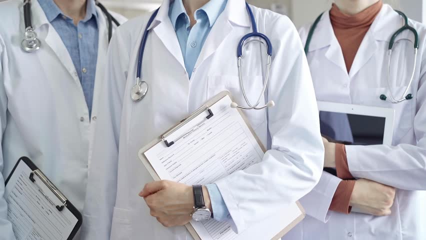 Group of doctors wearing white coats and stethoscopes standing with clipboards. Medical team at work