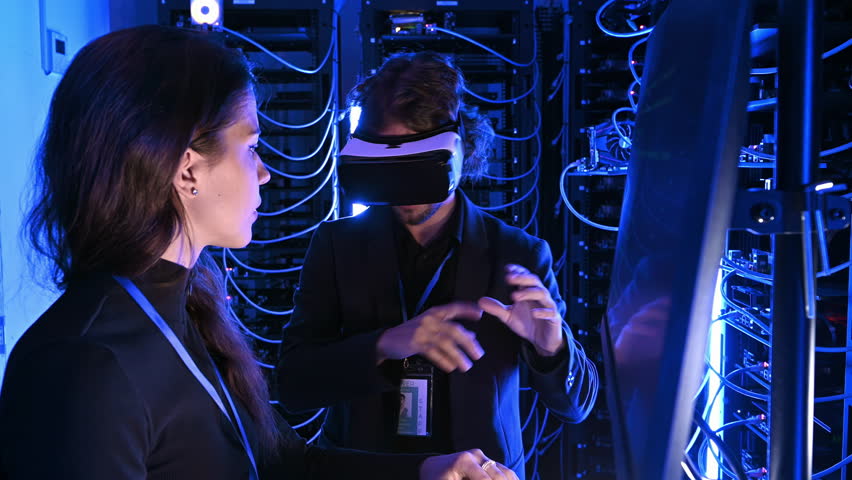 Woman programming in a server room while a man is using a Virtual Reality headset