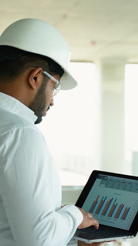 Indian Builder Engineer Using Laptop for Data Analysis at Worksite