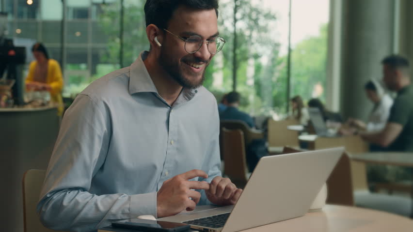 Smiling client tourist male guy Indian Arabian man businessman business worker in earphones chatting video call laptop conference meeting online friendly communicate in cafe computer distant studying