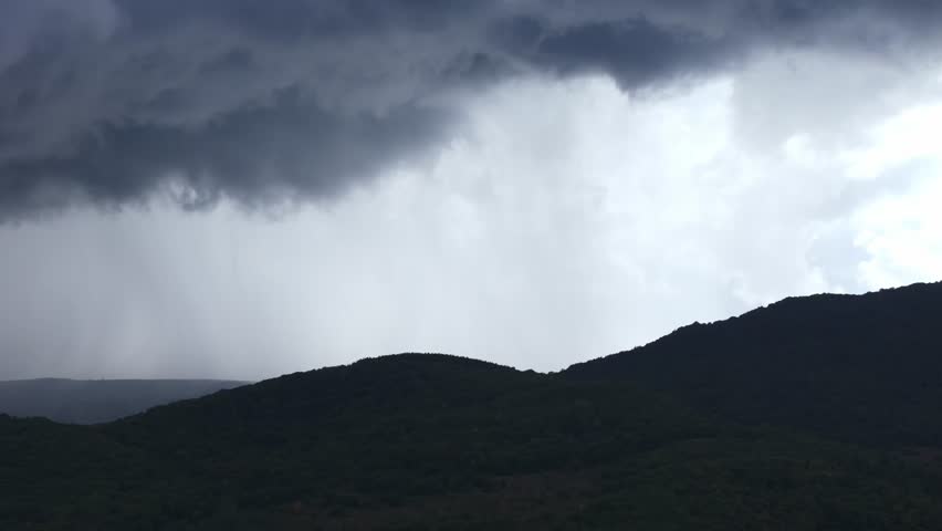 A dramatic rainfall over misty hills under dark clouds creates a mystical landscape