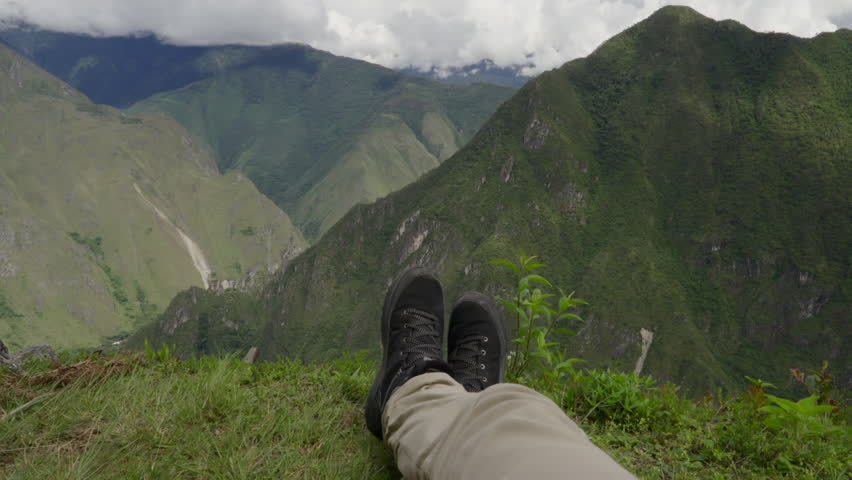 POV legs of explorer relaxing on top of Huayna Picchu mountain. Adventure, relax, wanderlust traveler