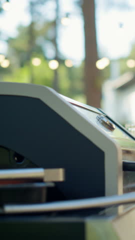 Vertical Screen: Close Up of a Man Grilling a Steak on a Barbecue in a Sunlit Garden with Friends Enjoying Drinks and Conversation in the Background. Warm and Inviting Outdoor Gathering Atmosphere