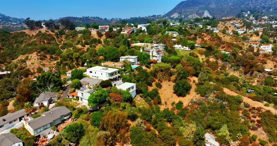 Multiple luxurious houses built on tops of the Hollywood Hills. Drone footage above the rocky panorama approaching Hollywood Reservoir. Los Angeles, California, USA.