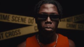 Young Black man with dreadlocks wearing gold accessories putting trendy sunglasses down his nose and looking seriously into camera at crime scene with flashing police lights. Video portrait - Powered by Shutterstock - Get 15% off with code: PIKWIZARD15