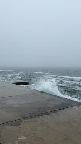 Misty Sea Waves: Choppy Waters Crashing Against City Concrete in Foggy Conditions