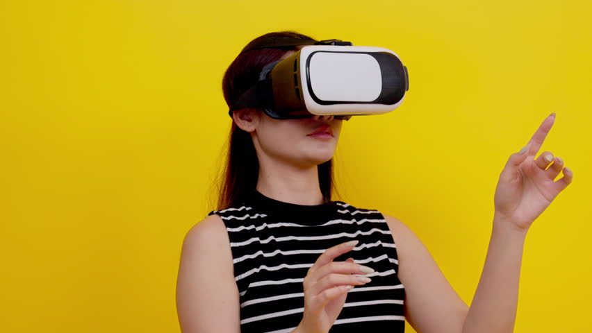 Asian young woman playing video games using mobile with headphones on yellow background isolated