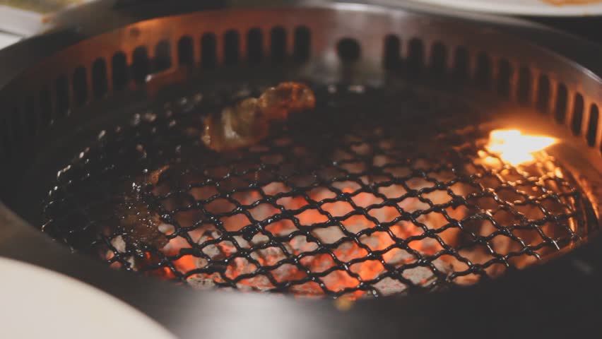 Grilled meat on a charcoal grill pan at Korean BBQ restaurant.