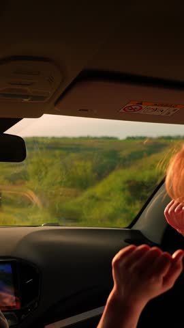 Female students driving in car listening to musical song on way sing and dance. Two happy women in car listening to radio, driving towards sun. Concept of youth, friendship, vacation travel at sunset
