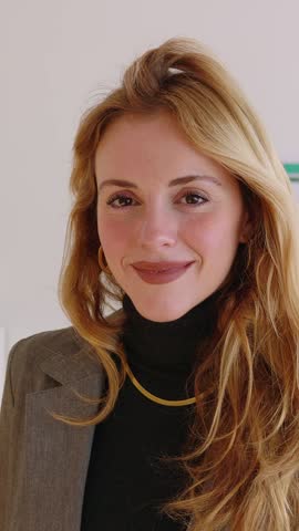 Vertical HD video portrait of young beautiful businesswoman looking at camera standing in the office. Front view of millennial professional female worker smiling. Business people concept.