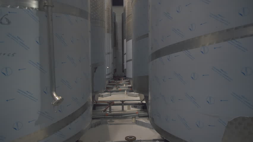 Multiple huge metal container tanks inside of the modern production facility. Big container tanks filled with produced alcoholic drinks. Container tanks with long tubes at the production factory.