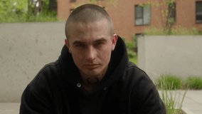 A young man with tattoos and piercings sits confidently, nodding to music. His serious, defiant gaze and folded hands exude dominance and toughness, reflecting a rebellious attitude in a city setting. - Powered by Shutterstock - Get 15% off with code: PIKWIZARD15