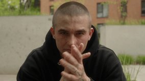 Tattooed man with piercings sits on steps, nodding to music while putting on his hoodie. His confident, rebellious expression, tough demeanor, and intense gaze reflect a dominant, defiant personality. - Powered by Shutterstock - Get 15% off with code: PIKWIZARD15