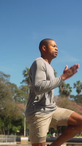 Determined African American man engaging in a vigorous high knees cardio exercise outdoors. Focused athlete pushing his limits during an intense workout under a clear blue, sky