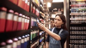 Young woman admiring and comparing vibrant paint colors in an art supply store. Smiling customer carefully selecting a paint tube, showcasing her creativity and passion for art - Powered by Shutterstock - Get 15% off with code: PIKWIZARD15