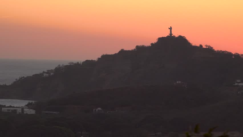 A statue of Jesus on a hill by the ocean during a beautiful sunset in San Juan del Sur