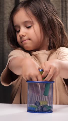 vertical video Little girl collecting old batteries in a recycling container
