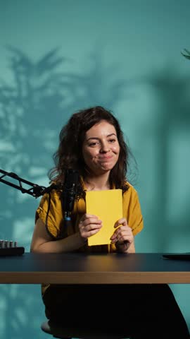 Vertical video Excited content creator films video review of book, browsing through pages, impressed by story. Online star giving her impressions of new novel release to readers, giving positive