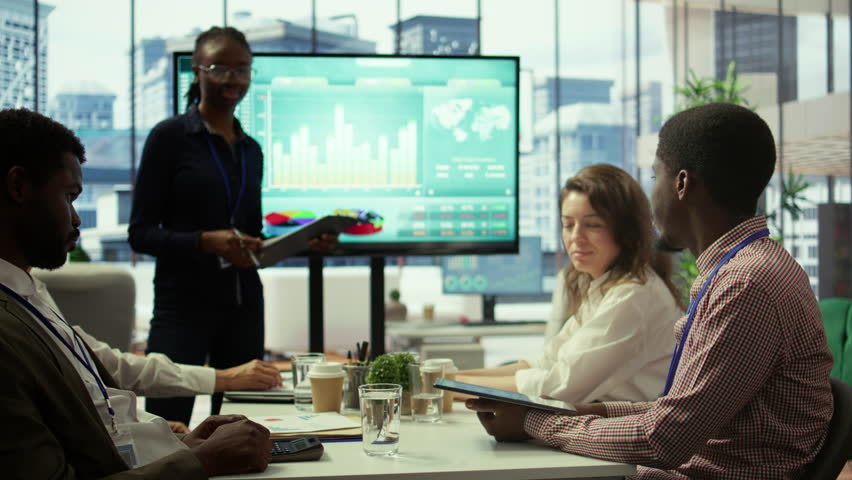 Diverse group of colleagues working together on allocating resources, attending a meeting in boardroom to review infographics and sales numbers on interactive board. Project management. Camera B. - Powered by Shutterstock - Get 15% off with code: PIKWIZARD15