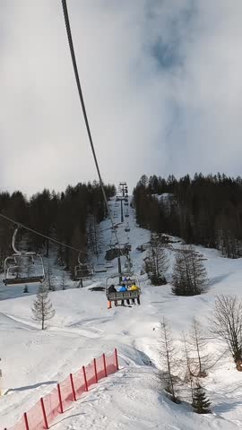 First-person view FPV point of view POV of cable chair ski lift ascend for alpine skiing in Dolomites. Ski resort piste with people skiing in Dolomites in Italy. Ski area Belvedere. Canazei, Italy