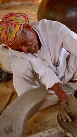 Indian potter at work: throwing the potter's wheel and shaping ceramic vessel and clay ware: pot, jar in pottery workshop. Experienced master. Handwork craft from Shilpagram, Udaipur, Rajasthan, India