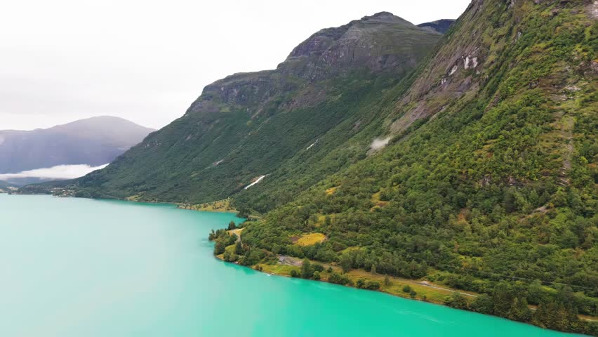 Aerial view of Lake shoreline of Lovatnet in Norway, showcasing turquoise waters surrounded by mountains and forests