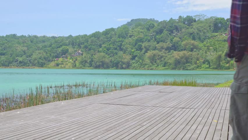 Man on a wooden platform by the lake. A man standing on a wooden platform by the lake, looking out at the serene landscape. He is enjoying the beautiful scenery and the tranquil atmosphere.