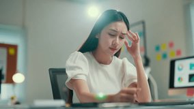 Young asian businesswoman is massaging her temples, trying to relieve a painful headache. She is sitting at her desk in her office - Powered by Shutterstock - Get 15% off with code: PIKWIZARD15