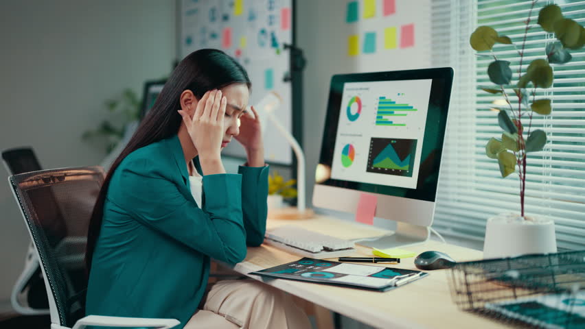 Young professional woman is having a headache while working at her desk. She is massaging her temples trying to relieve the pain