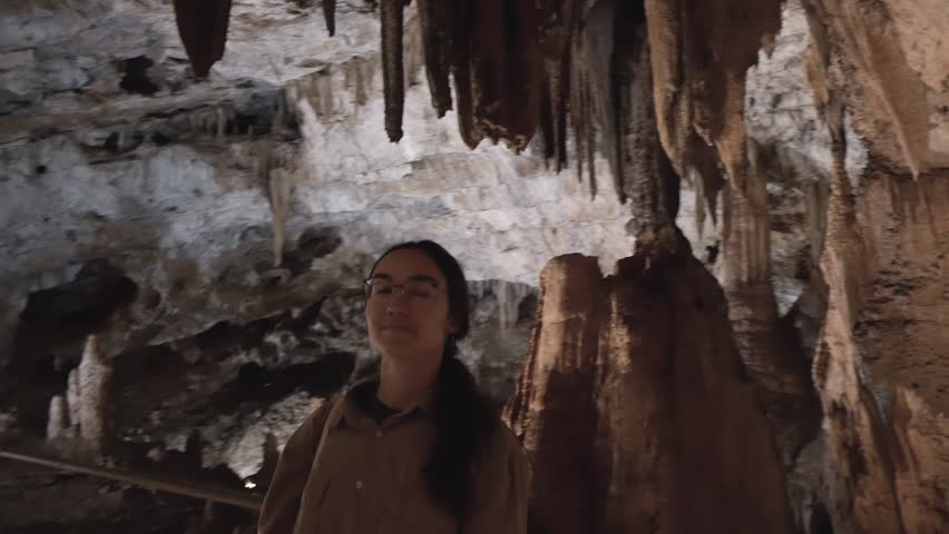 Beautiful young female tourist exploring rock formations in an ancient cave.