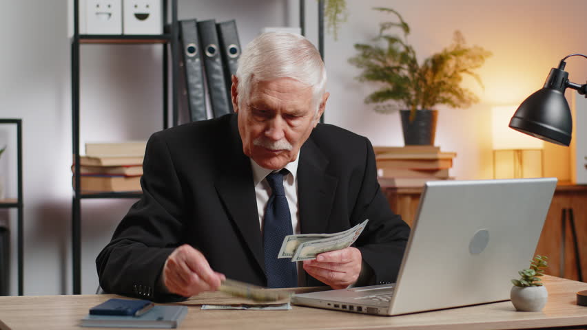 Rich grandfather businessman working on laptop counting money dollar cash, calculate earnings income profit at home office workplace. Professional freelancer. Business people. Employment occupation