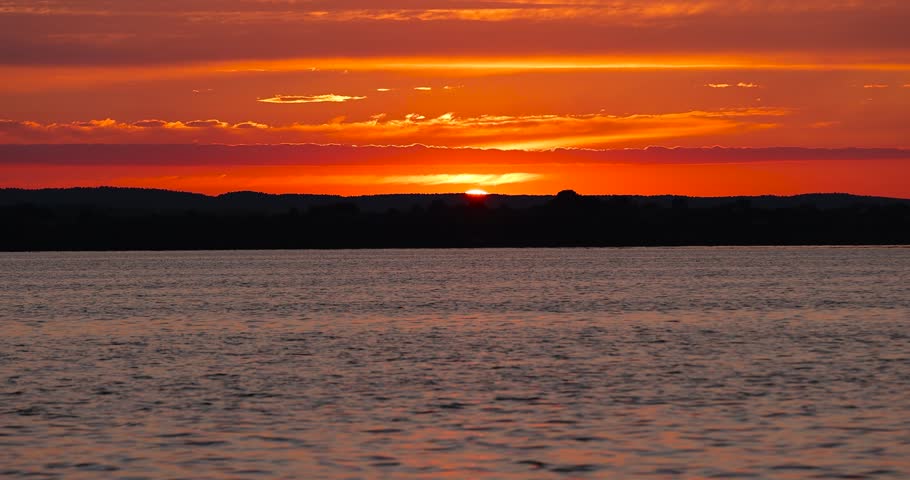 sunset with sun and orange sky on the lake, reflection of the orange sky in the waves on the lake during sunset