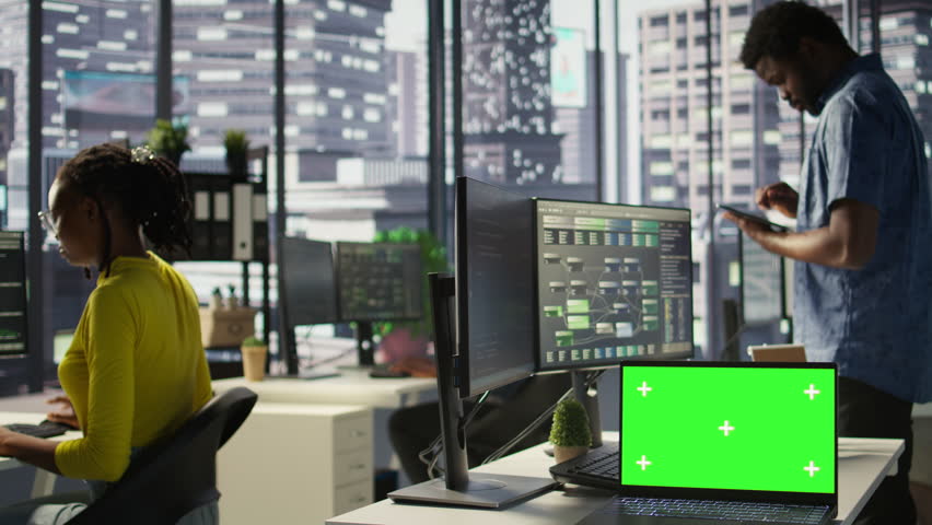 Green screen laptop on desk in workspace with admins in background doing software quality assurance. Chroma key notebook in office with woman at work inspecting coding on device, camera B