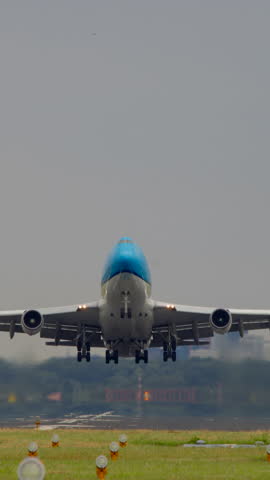 Vertical video of a large commercial airplane taking off from the runway, with clear skies and green surroundings