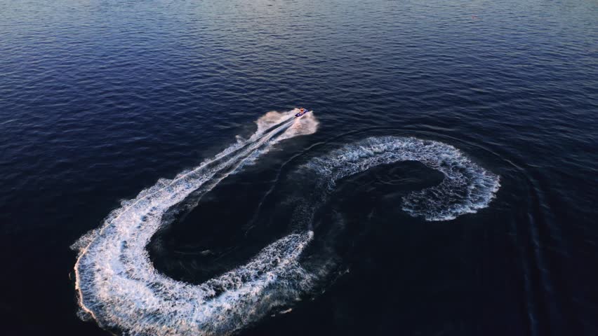 From a bird's eye view, a jet ski races at high speed in the clear sea water. Krk island, Kvarner bay, Croatia, Europe. Cinematic aerial shot. Discover the beauty of earth. Filmed in 4k, drone video.