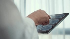 Unrecognizable doctor reviews and analyzing patient brain x-ray scan on digital tablet. Doctor Diagnosis with brain X-ray image on Digital Tablet. - Powered by Shutterstock - Get 15% off with code: PIKWIZARD15