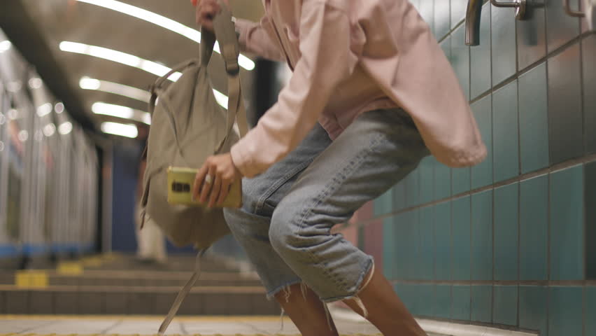 Young girl in stylish clothes with a backpack waiting for a train at the metro station. Girl waiting for a train. Girl in the metro.