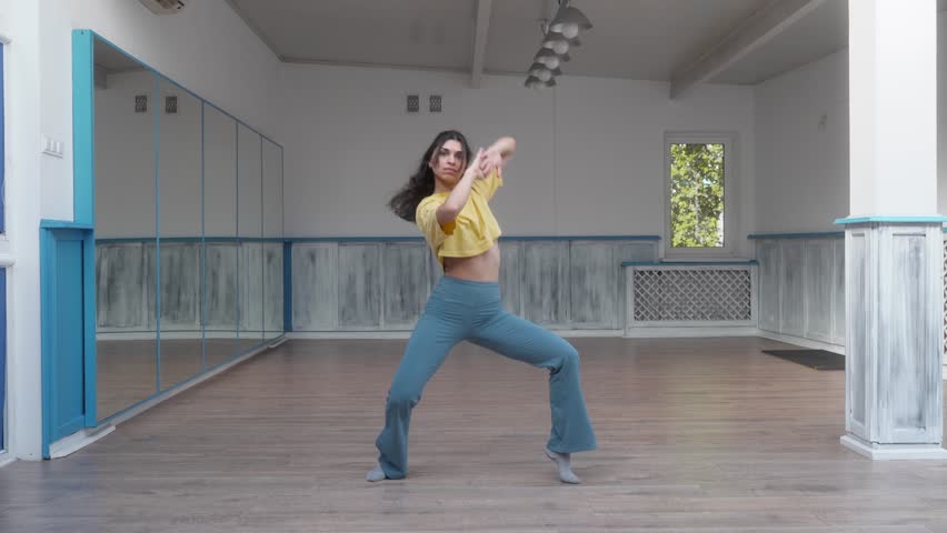 Dancer gracefully performs fluid and elegant movements in a dance studio. Soft gestures and smooth transitions highlight femininity and control. The choreography emphasizes flow and balance.