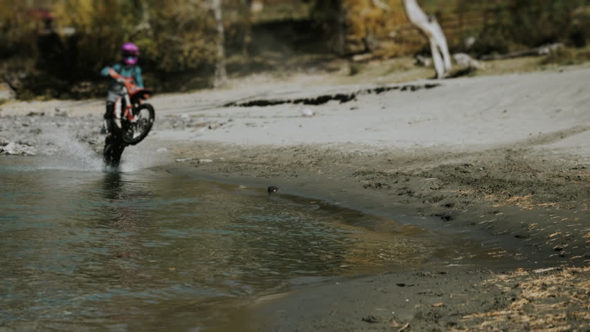 An enduro rider rides on the back of a motorbike along a mountain river. Water splashes in different directions from the motorcycle wheels. Riding a motorcycle along a mountain river.