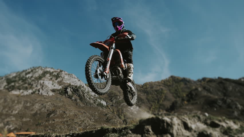 Enduro racer jumping on a motorcycle from a cliff against the backdrop of beautiful mountains. A racer jumps on a motorcycle. Extreme bike riding in the mountains.