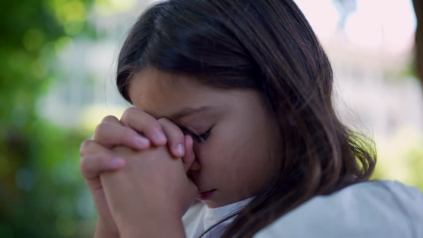 Girl clasping her hands together, eyes closed in deep concentration, evoking a sense of spirituality, hope, and faith. peacefulness in a natural setting