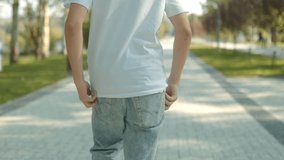 A adolescent in a white T-shirt and jeans walks outdoors in a park on a sunny day, pulling out his phone from his pocket as he enjoys the fresh air and natural surroundings. - Powered by Shutterstock - Get 15% off with code: PIKWIZARD15