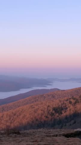 A vertical shot of the Smoky Mountains in Tennessee at dusk, featuring soft pastel hues over rolling hills and a tranquil lake, perfect for scenic landscape visuals.