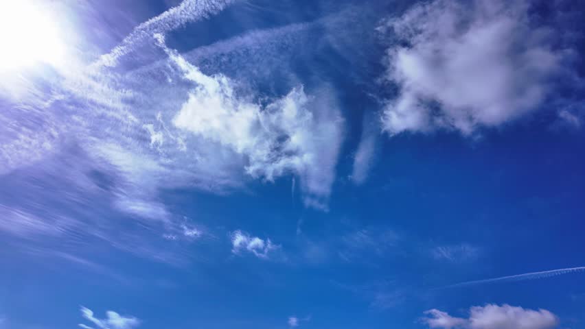Vivid blue sky with wispy cirrus clouds and contrail, daylight, atmospheric timelapse