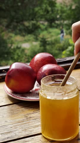 Apples red whole and sliced with a jar of honey on the traditional Jewish holiday of Rosh Hashana on a wooden table by the window on a sunny day. Close-up, vertical